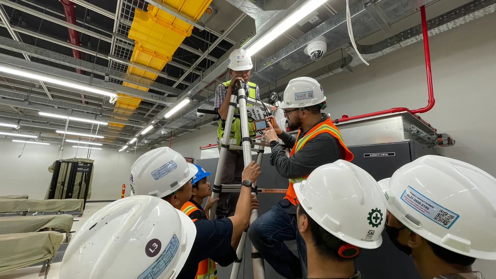 Optima Dewata Energi engineers measuring airflow above a CRAH unit inside a data hall